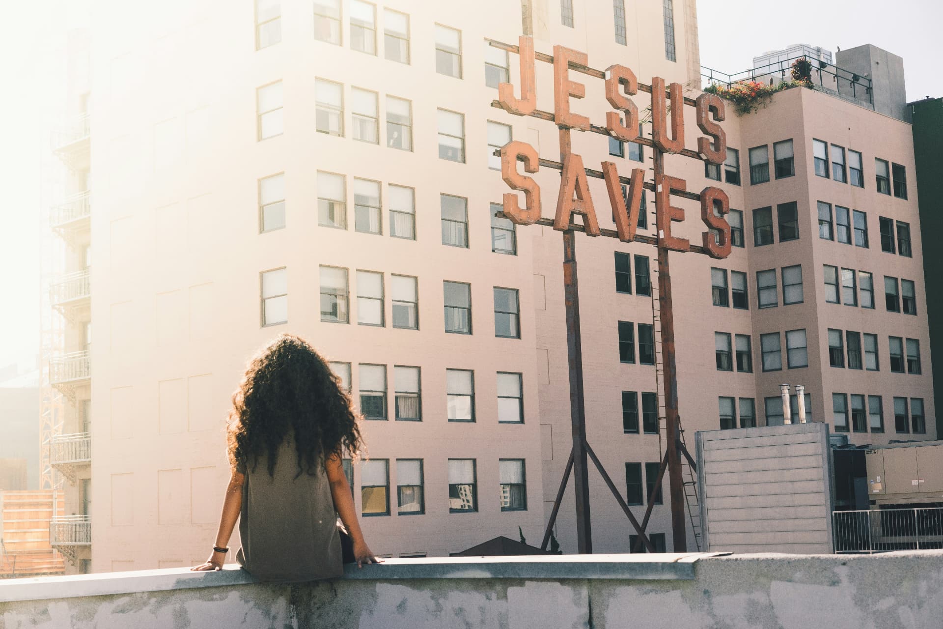 A woman on a rooftop looking at a large Jesus Saves sign