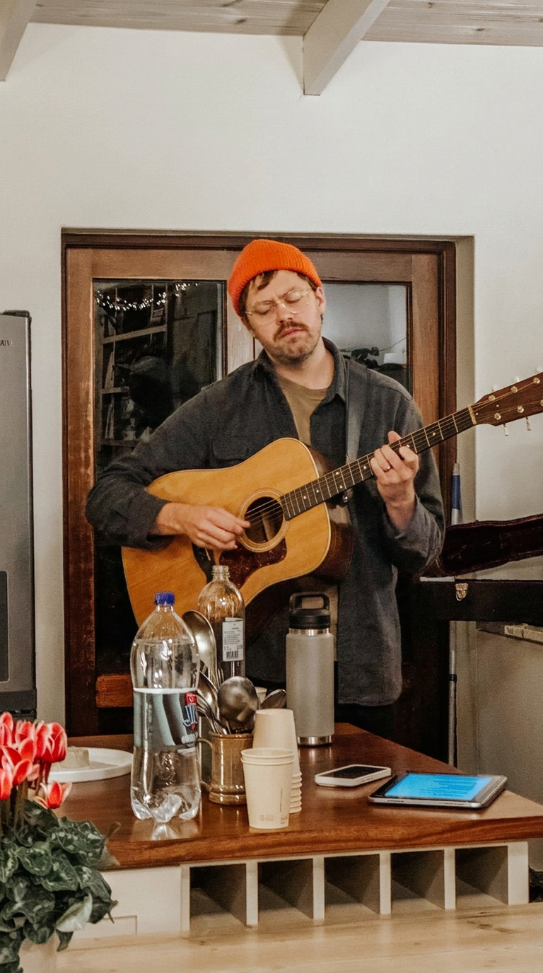 A man in a beanie leading worship on acoustic guitar in a kitchen